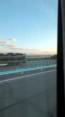 The video shows the interior of a bus traveling at sunset. The camera is positioned low down, looking up towards the front of the bus. The seats in the bus are visible, as are curtains along the windows. Through the windows, a sunset can be seen with a bright orange glow. Several passengers are seated on the bus, some facing forward and others to the side. One passenger in the foreground is partially visible. The bus appears to be moving, indicated by the slight blur of the scenery outside.