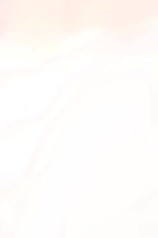 A blurry video begins focused on the corner of a room, then quickly pans up to reveal a wall with a green pipe attached. The camera moves quickly to show a person sitting down, wearing a pink shirt and gray shorts. Their face is slightly obscured by their arms in front of them. The video ends with a pale blurry wall.