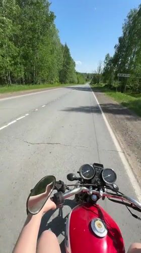 Motorcyclist rides red bike on tree-lined road near Zhigalki