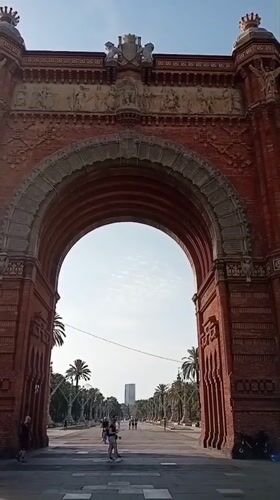 Ornate brick arch opens onto a shaded Barcelona promenade