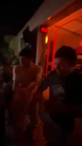 The video shows a group of people dancing in a bar or club setting. The lighting is dim and red, creating a party atmosphere. There's a bar visible in the background, with several people gathered around it. The focus is on the individuals dancing, although the camera moves around, catching glimpses of other patrons. One woman wears sunglasses. The crowd seems to be enjoying themselves, moving to the music.