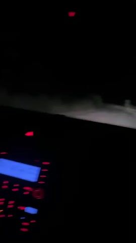 The video shows the interior of a car at night. The headlights illuminate a dirt road ahead, with some vegetation on either side. The car's dashboard lights are visible, with red and blue illumination. The vehicle appears to be in motion.