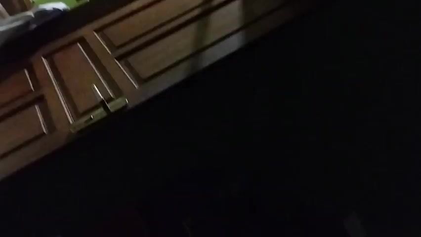 Here's a forensic description of the video:

The video starts with a very dark view, with only a small portion of a wooden door visible in the upper left. The door appears to have a brass handle. As the video progresses, the angle shifts, revealing more of the door and a glimpse of a bed with white sheets in the background. The majority of the frame remains dominated by darkness. No people, actions, or interactions are visible. The environment appears to be a dimly lit room.