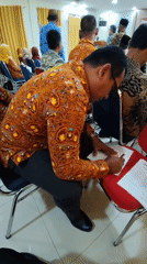 Indoor formal gathering in batik and peci attire at a local venue