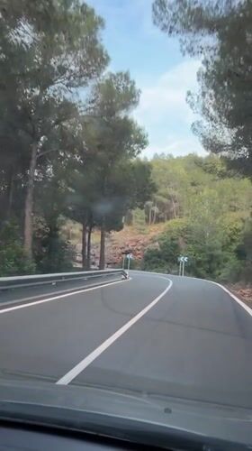 Vehicle travels winding tree-lined road in Serra, Spain