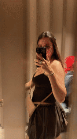 Woman takes mirror selfie, exits as second woman enters hallway