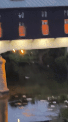 Littered waterway in Lovech reflects bridge and building lights