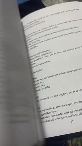 The video shows an open book with pages being flipped. The book appears to be a technical or programming textbook, with text, code snippets, and diagrams visible on the pages. The camera is focused on the book as it is handled, with the background blurred. The lighting is somewhat dim, suggesting an indoor setting. The pages of the book are white with black text. The book is lying flat on a surface, and a hand is visible briefly flipping the pages. The content of the pages includes discussion of paradigms, message handlers, and code related to mathematical operations and calculations. There are also tables and diagrams. The book has page numbers visible, such as 100, 101, and 31. The video appears to be a short recording, possibly showing a demonstration or a review of the book.