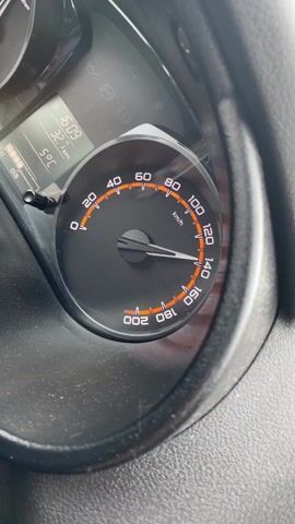 The video shows a close-up of a car's speedometer. The speedometer needle fluctuates between approximately 100 and 120 km/h. A digital display next to the speedometer shows the time as 16:09, a distance of 32.8 km, and a temperature of 5°C. The car's dashboard is visible as a dark-colored, slightly dusty surface.