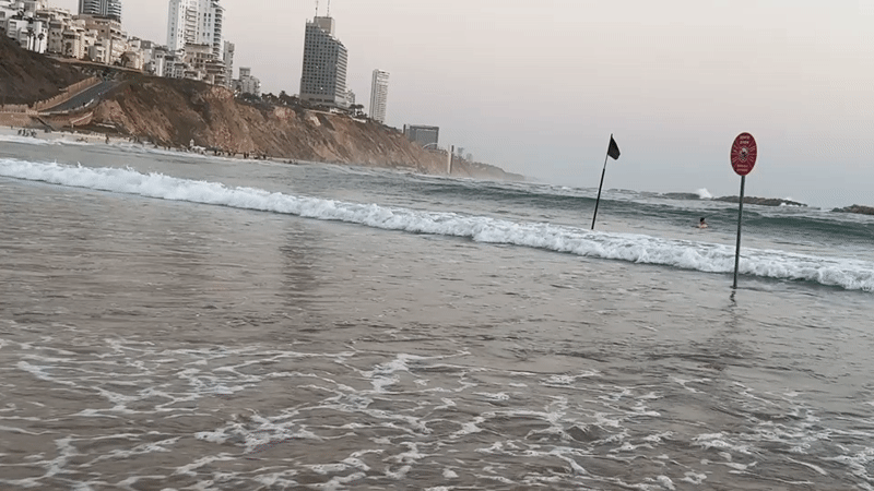 Netanya beachfront with cliff buildings and flagged surf poles