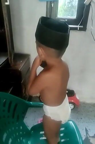 Toddler on a plastic chair, snacking indoors in North Aceh