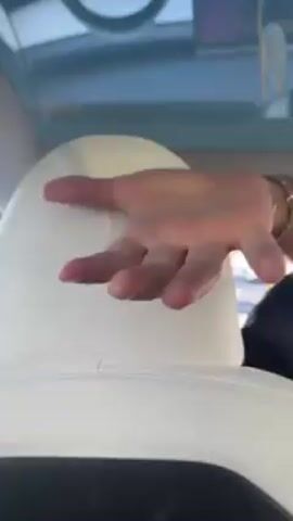 The video shows the inside of a car, a Tesla, with a man in the driver's seat. He is wearing a black shirt and a bracelet. His hand is tapping on the back of the white headrest. The infotainment screen is visible, as is traffic outside the car. Music is playing.