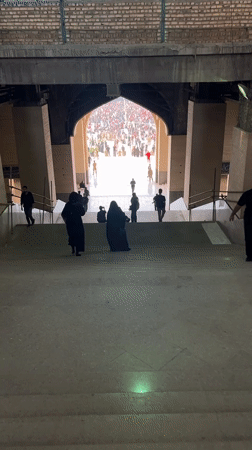 Crowd flows down a grand staircase toward an arched hall in Tehran