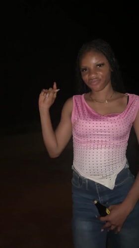 Woman dances with bottle during nighttime gathering in Ogbe