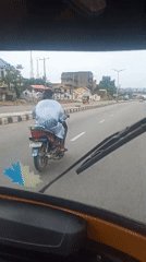 Motorcyclist in striped shirt travels paved road in Lokoja