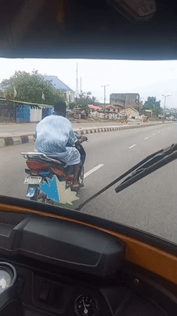 Motorcyclist in striped shirt travels paved road in Lokoja