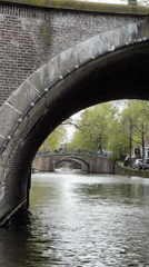Canal boat cruise navigates Amsterdam waterways on overcast afternoon