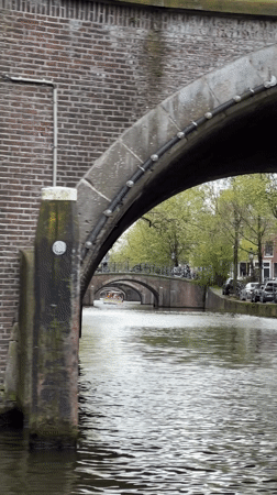 Canal boat cruise navigates Amsterdam waterways on overcast afternoon