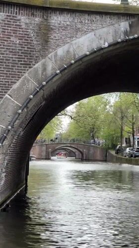 Canal boat cruise navigates Amsterdam waterways on overcast afternoon