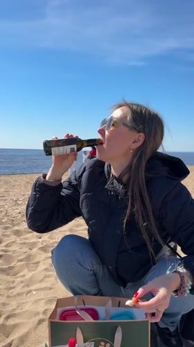 Woman drinks from wine bottle on Russian beach