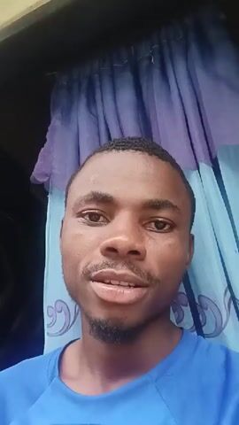 This media file is a close-up, head-and-shoulders shot of a young Black man speaking directly to the camera. He has dark skin, short dark hair, and a goatee. He is wearing a blue t-shirt. The background consists of curtains that appear to be a mix of purple and light blue, with a decorative pattern. The lighting suggests it is daytime, though the exact time of day is unclear. The setting seems to be indoors, given the presence of the curtains.

The man is engaged in conversation, with his mouth open as if speaking. His expression is engaged and he appears to be expressing thoughts or opinions. The video is framed from the chest up, with the man's face being the central focus. The overall tone is conversational and personal. There is no visible text in the media file. The location context provided is Afaha Ukwa, Nigeria, which adds a cultural and geographical layer to the subject's appearance and the setting.