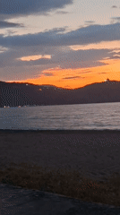 Sunset documented over ocean beach with mountain silhouette backdrop