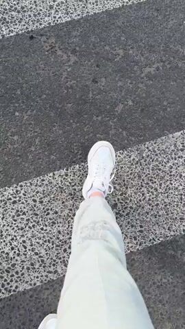 The media captures a street scene in Rubtsovo, Russia, on a bright, sunny day, indicated by the clear blue sky and strong shadows. The primary activity is pedestrian and cyclist movement across a pedestrian crossing.

The footage begins with a low-angle shot of a person's legs wearing light-colored pants adorned with shimmering silver sequins and white sneakers, stepping onto a crosswalk. The crosswalk itself is characterized by alternating white stripes and dark asphalt, appearing somewhat worn.

The scene then broadens to show two individuals on bicycles traversing the same crosswalk. The first cyclist, a woman with dark hair wearing a dark t-shirt, is riding a bicycle with a dark frame. Following her is a man in a bright blue t-shirt with white text, also on a bicycle. Both are riding through the pedestrian crossing.

In the background, residential buildings and trees line the street. The architecture suggests an urban or suburban environment typical of Russian cities. Several cars are visible on the road, indicating moderate traffic. One car, a dark SUV, is stopped at the crossing, presumably for the cyclists. Another dark SUV is moving away from the camera. Further down the road, a lighter-colored car is also in motion. A traffic light can be seen in the distance.

The overall impression is a slice of everyday life, capturing people navigating a city street on a pleasant day. The presence of the sequined pants adds a touch of personal style to the pedestrian. The clear weather and daylight setting suggest the activity is taking place during the daytime.