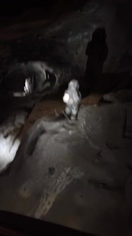 The video captures an interior view of a dimly lit underground passage, likely within a mine or cave. The environment features dark, rough-hewn walls, appearing to be natural rock or salt formations. Artificial spotlights strategically illuminate sections of the walls and the path ahead, creating dramatic contrasts of light and shadow.

Prominent wooden structures are integrated into the underground setting. These include sturdy wooden pathways, ramps, and support beams, indicating a well-constructed route for visitors.

Several people, dressed in casual attire, are visible throughout the passage. They appear to be tourists or explorers, navigating the wooden walkways and moving downwards into the depths of the underground system. The camera, held by someone moving through the mine, offers a first-person perspective of the descent, panning to show the verticality and scope of the cavernous space.

The activity primarily involves walking and exploring the extensive underground network. The setting suggests an established tourist attraction, designed to allow safe passage through a naturally impressive or historically significant underground location. No text is visible in the video.