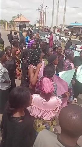 This video captures a daytime protest in Ungwan Tanko, Nigeria, involving a large group of men and women, primarily women. The participants are gathered on what appears to be a roadside, holding various handwritten signs and actively vocalizing.

The signs reveal the nature of their grievances:
*   Several signs, both green and white, prominently display the text: "FROM AUGUST TO MAY NOTHING HAS BEEN DONE ABOUT OUR CROPS." This indicates a problem with agricultural produce, potentially lack of compensation, destruction, or inaction by authorities over a long period.
*   Other signs, in pink and green, read: "NO PAYMENT NO WORK," suggesting that they are either demanding payment for work already done or refusing to work due to lack of payment, possibly related to the crop issue.
*   A white sign clearly states: "ENOUGH IS ENOUGH," conveying widespread frustration.
*   Another partially visible green sign asks: "HOW DO YOU WANT US TO LIVE WITHOUT CROPS?" directly highlighting the impact of the agricultural problem on their livelihoods.

The crowd appears agitated and determined, with some individuals speaking loudly or chanting. Cars are visible in the background, suggesting a public road or intersection. The setting includes power lines overhead, simple roadside buildings, and some trees, indicating a semi-urban or rural environment. A man wearing a "cellulant" cap and carrying a camera is seen among the protesters, possibly documenting the event. The atmosphere is tense but organized, characterized by collective action to draw attention to their demands regarding their crops and financial compensation.