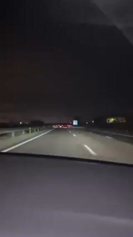 The video shows a car driving on a highway at night. Headlights from other vehicles and signage are visible in the distance. The interior of the car is visible, with the dashboard and air vents in view.