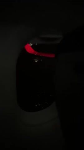 This video shows a view from an airplane window at night. The frame is mostly dark, with the faint lights of a city visible on the horizon below. In the upper part of the frame, near the edge of the window, there are some illuminated objects that appear to be reflections on the windowpane. These reflections shift and change slightly as the plane moves.