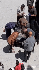 Men move metal drum while mechanic services commercial vehicle