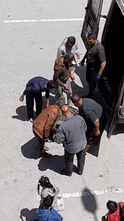 Men move metal drum while mechanic services commercial vehicle