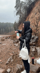 Woman visits rocky shoreline near Kostovaty, Russia on overcast afternoon