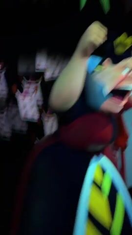 The video begins with a blurry, dark shot that appears to be a person holding a camera and pointing it towards a display. The display is of a white figure with blue accents and a green object in the background. The camera pans to the right, showing more of the display, which seems to include several small, pink and white objects. The video then shifts to a very blurry, animated, red and white figure with a heart symbol on its chest, appearing to be a playing card character. The camera continues to move, showing another blurry, animated figure, this time more abstract, with red accents and a pinkish-purple face, also appearing to be a playing card character. The final shot shows the camera moving down a dark hallway with light shining from the end. The hallway walls are decorated with projected images, including a large, blue and black spiral pattern.