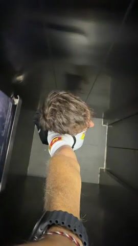 A person takes a first-person view video in an elevator. The shot is from above, looking down at their head, arm and the elevator floor. A poster advertising a "Whale Shark Expedition" is visible on the elevator wall. The elevator is moving upwards, as evidenced by the changing floor numbers on the elevator panel.