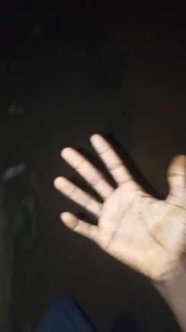 A first-person perspective video shows a hand held up to the camera at night. The hand is partially illuminated, and the background is dark and indistinct, possibly indicating an outdoor setting. The hand is open, with fingers spread. The video is shaky and moves around slightly.
