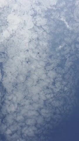 A drone flies toward the camera under a cloudy sky.