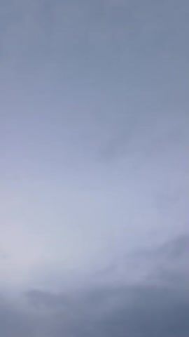 This is a vertical video of a cloudy sky. There are thin, dark horizontal lines that appear to be power lines across the lower portion of the frame. The clouds are a light gray and white, and the sky transitions from a lighter shade at the top to a darker shade at the bottom. The video is only four seconds long and contains no discernible audio.