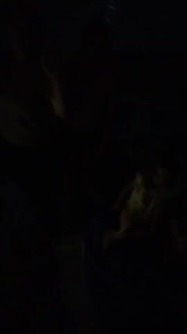 The video is of a concert. People are in a dark setting. A person with a yellow shirt is seen on the left of the screen. Another person with a light-colored shirt is seen in the center. The concert appears to be energetic, with people moving. There are flashing lights and a lot of movement in the crowd.