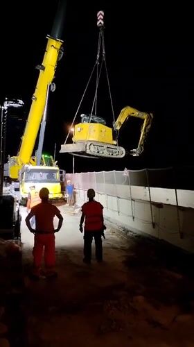 Night crane operation lifts excavator at Italian construction site