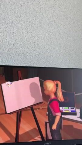 A blonde-haired doll with a ponytail, wearing a pink shirt and denim overalls, stands in front of a blank canvas on an easel. She holds a paintbrush in her right hand. A palette of paints sits on a table to her right. The doll then turns and faces a painting of a seascape with colorful clouds. She gestures towards the painting with her paintbrush. The scene appears to be animated.