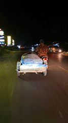 Motorcyclist transports covered cargo through Lhokseumawe at night