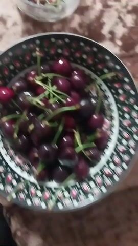 A bowl of cherries is shown in a close-up shot. The bowl has a black and white patterned rim with red accents. The cherries are dark red and have green stems. The video is static and does not show any action.
