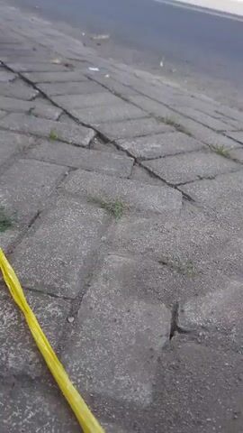 A yellow ribbon lies on cracked concrete paving stones next to a road. A car drives by on the road.
