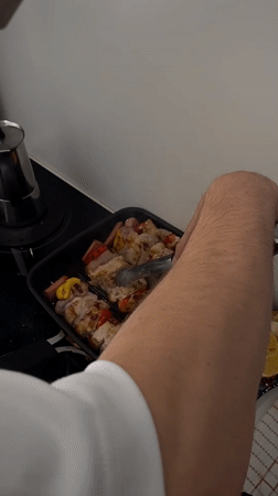 Person cooks meat and vegetable skewers in Milan kitchen
