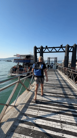 Tourist walks pier among dive boats in Rawai harbor