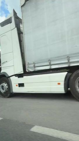 The video shows a gas tanker truck being inspected by two people wearing high-visibility vests. The truck is white and has markings indicating it contains a flammable substance. The inspection is taking place on the side of a road. A white car with "RIA" printed on it is parked nearby. Several other vehicles with agency logos are parked off the side of the road. The sky is partly cloudy.