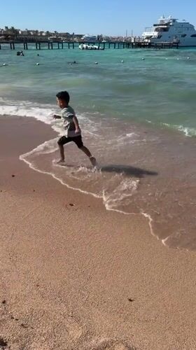 Boy runs along Egyptian beach as yacht docks at pier