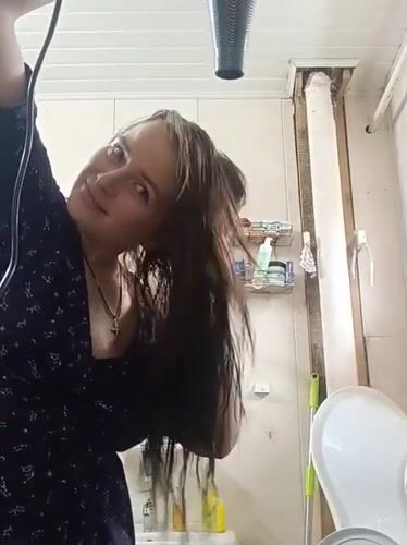Woman blow-dries hair in bathroom in Rusalevka, Russia